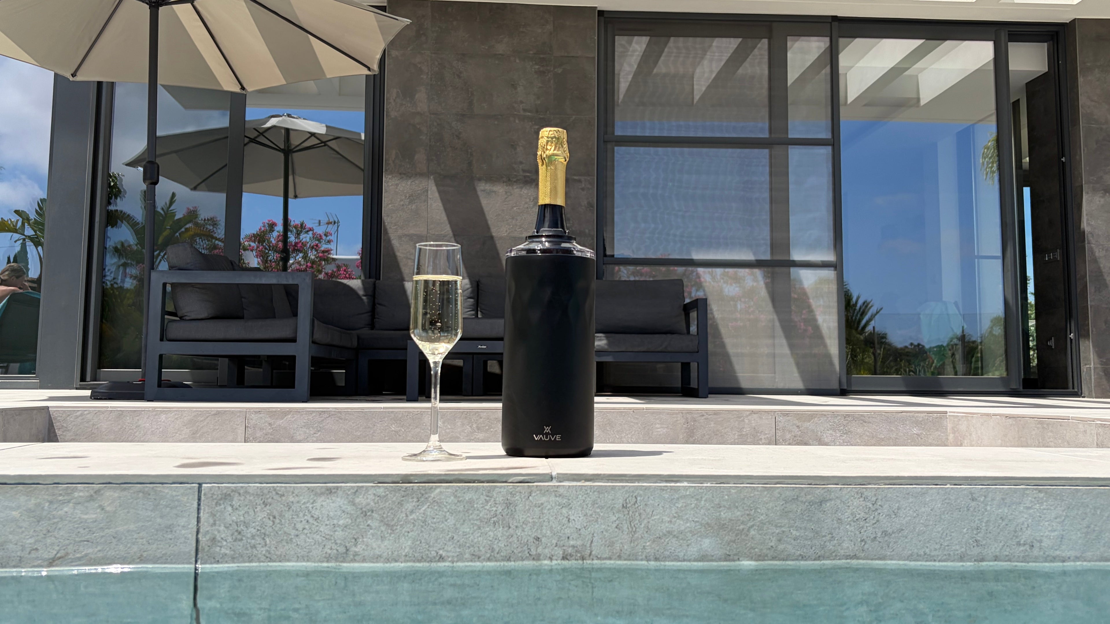 Bottle of champagne with a glass by a poolside in a modern outdoor setting